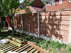 Waney lap fencing panel, with plain concrete bargeboards, during construction.