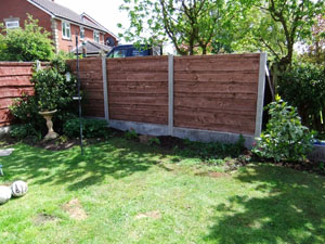 Waney lap fencing panel, with plain concrete bargeboards, during construction and nearing completion.