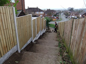 Vertical Close Board fencing panel, with plain concrete bargeboards, during construction and nearing completion.