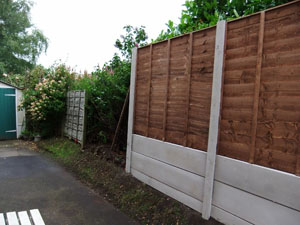 Waney lap fencing panel, with plain concrete bargeboards, during construction.